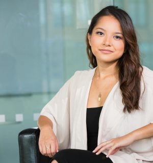 A professional Asian businesswoman sitting confidently in a modern office setting.